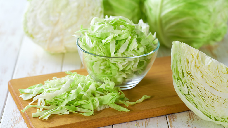 Chopped cabbages in a clear bowl and on a wooden chopping board