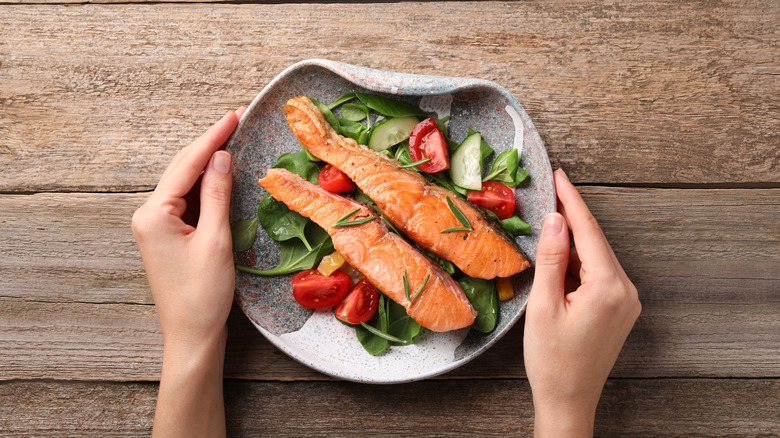 A plate containing two pieces of salmon along with fresh spinach tomatoes, and cucumbers