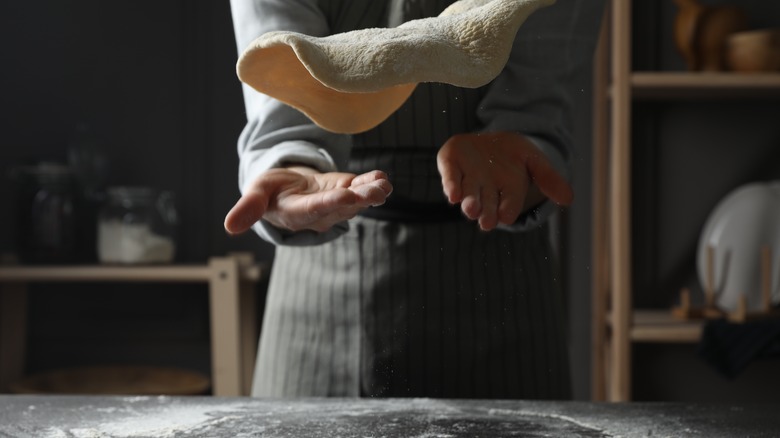 A woman tossing a pizza dough at a table in a kitchen.