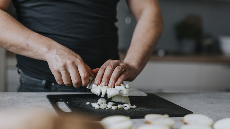 Person chopping onions on a black chopping board
