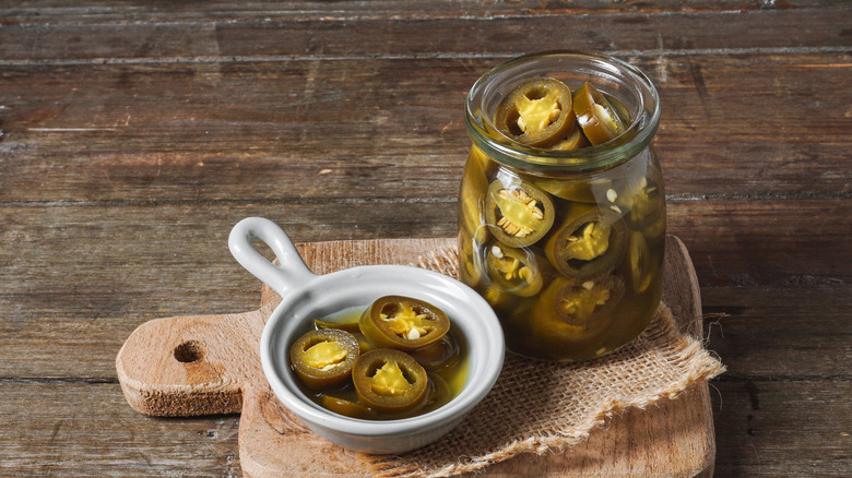 A jar and a dish of pickled jalapeños on a cutting board
