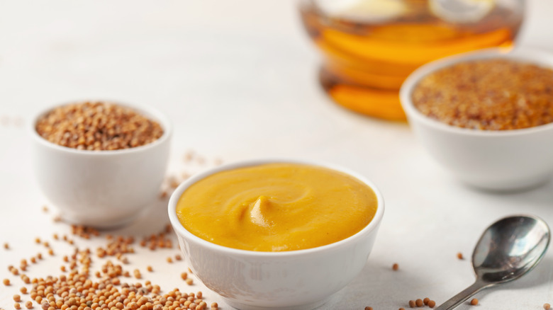 honey mustard in a small serving cup with honey and mustard seeds in the background