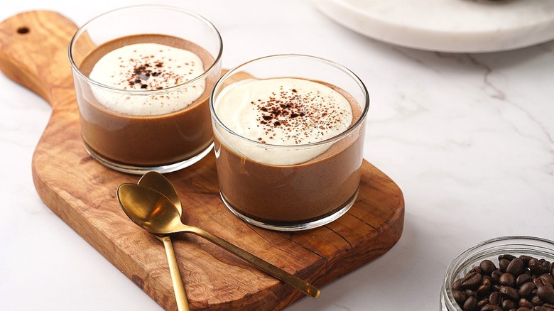 Coffee mousse dessert in two small glass cups atop a wooden serving board