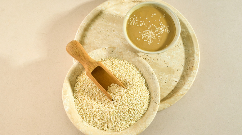 A small bowl of tahini and a larger bowl of sesame seeds are side by side.