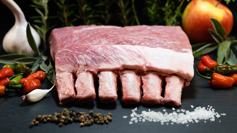 A rack of uncooked Duroc pork ribs arranged with herbs and spices.