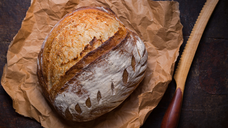 Overhead shot of baked sourdough bread on a paper sheet with a knife.