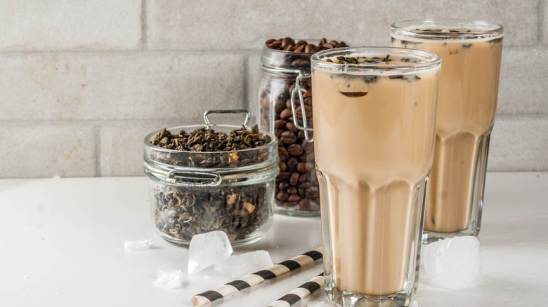 Glasses of iced yuenyeung surrounded by a jar of coffee beans and tea leaves.