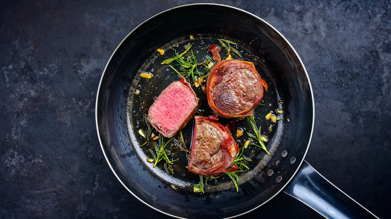 Bacon-wrapped filet mignons cooked to medium-rare in a pan.