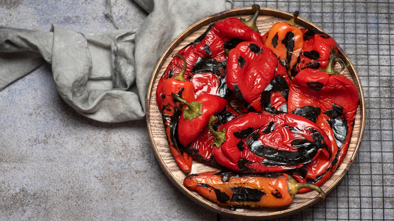 Roasted red peppers with stems on a round, wooden plate