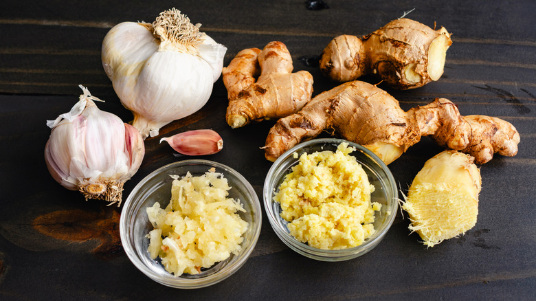 Prep bowls filled with grated garlic cloves and ginger root on a wooden table.