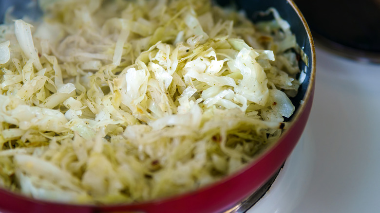 Chopped cabbage is photographed in close-up in a pan on a stove.