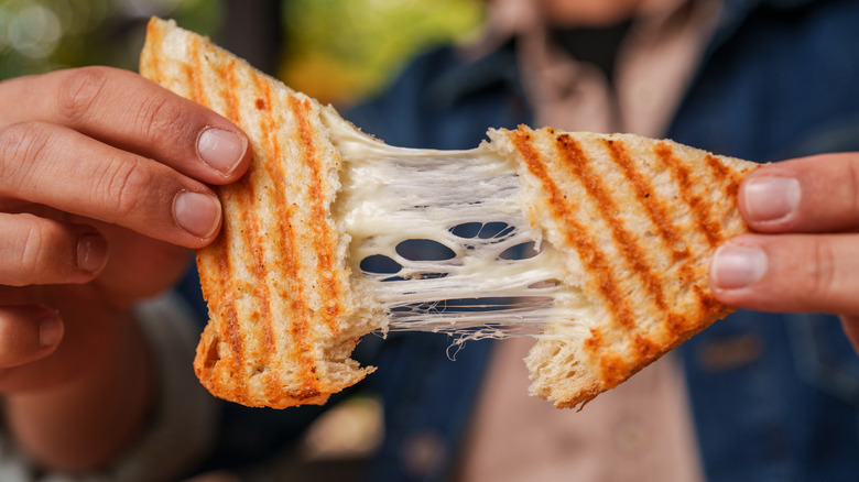 Person pulling apart a grilled cheese sandwich with strings of melty cheese connecting the two pieces
