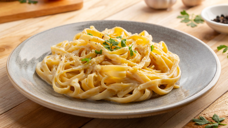 Creamy fettuccine garlic pasta topped with parsley and parmesan cheese in a plate.