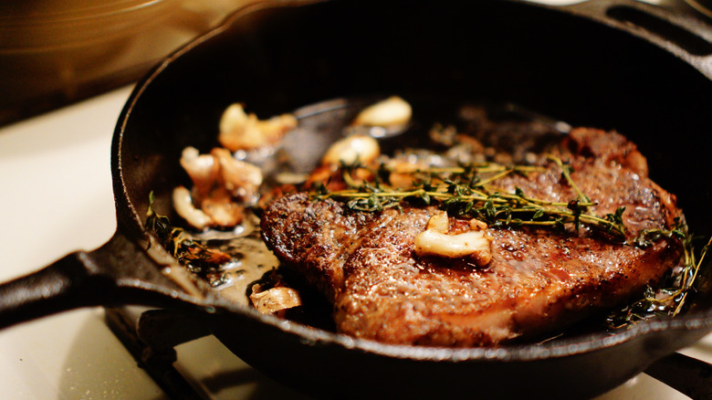 Steak cooks in a cast iron pan with garlic and herbs.