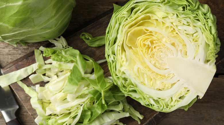 Fresh cut cabbages and knife on wooden table, flat lay