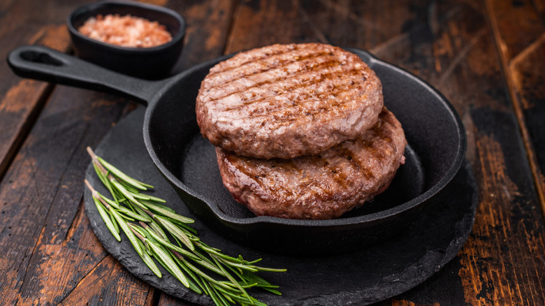 beautifully grilled burgers sit in a cast iron skillet