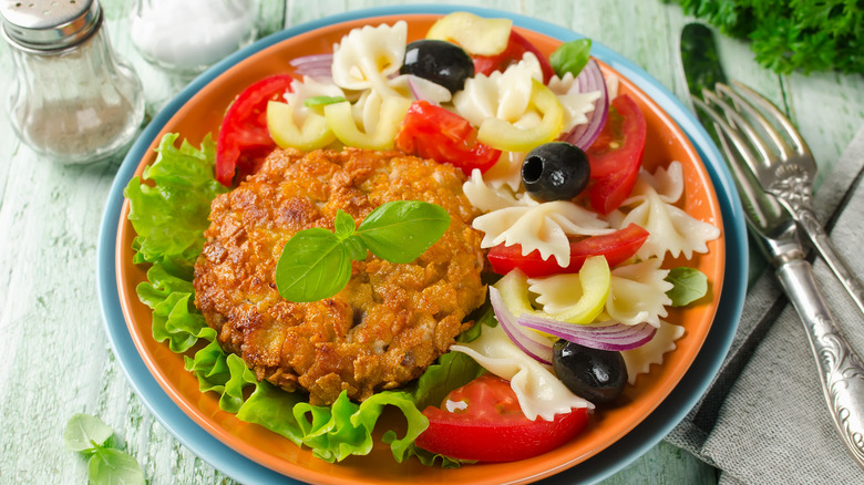 Cornflake-crusted pork chops on a plate with pasta salad and garnish