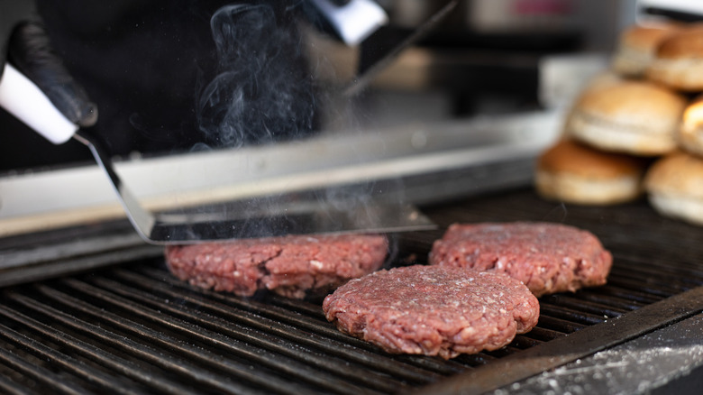 Burgers being cooked over a flame on a grill grate
