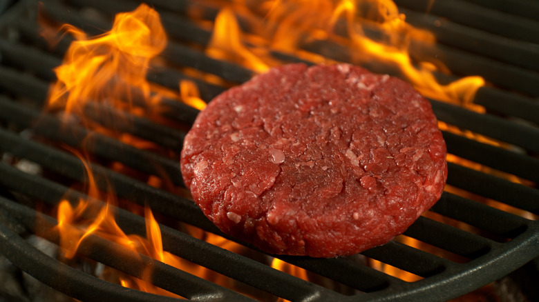 Close-up of a beef patty on a grill with roaring flames.