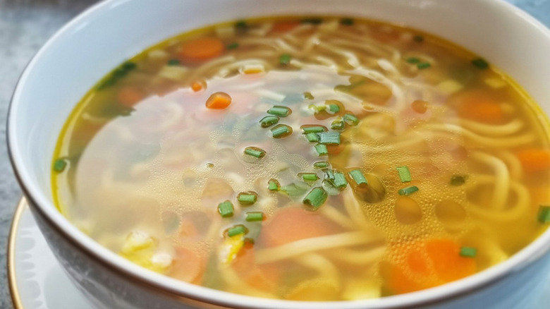 Chicken noodle soup in a white bowl topped with chives.