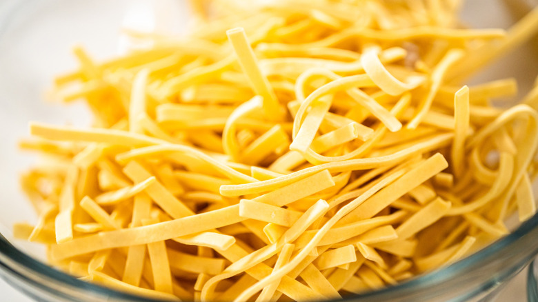 Close-up photo of dry kluski noodles in a glass bowl.