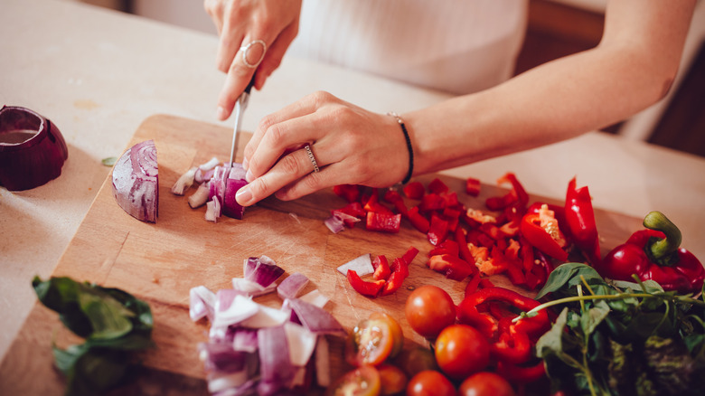 Person cutting onions, red bell peppers, and tomatoes
