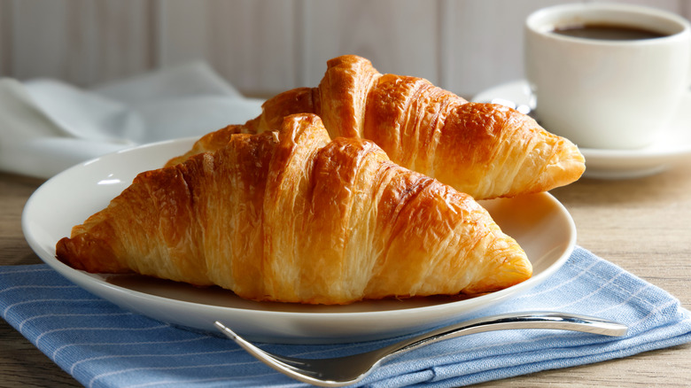 Two croissants on a plate with a fork and cup of coffee
