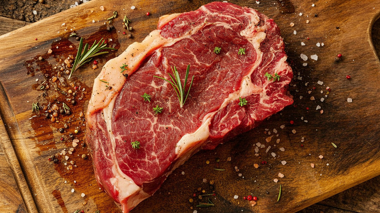 raw ribeye steak seasoned on a wooden cutting board