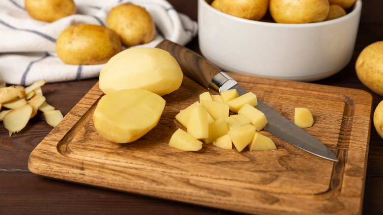 Whole and cubed potatoes on a wooden cutting board.