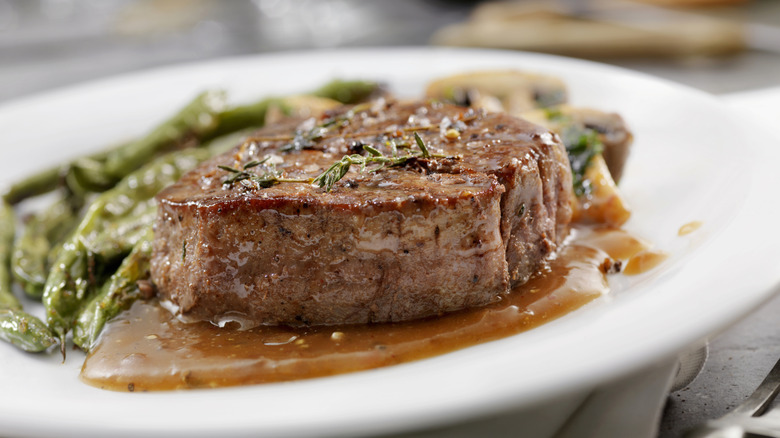 A filet mignon on a plate with sauce and greens.