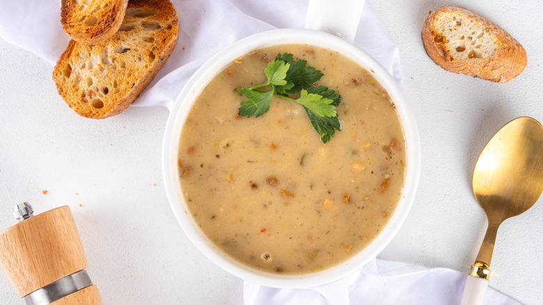 Soup in a white bowl with pieces of bread next to it on a table