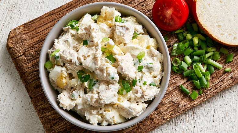 A bowl of chicken salad on a wooden board with chopped spring onions