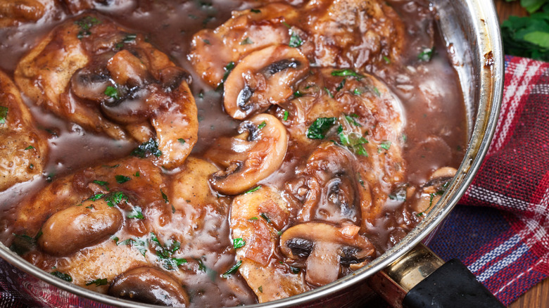 Marsala sauce is cooking in a pan, with mushrooms and herbs.