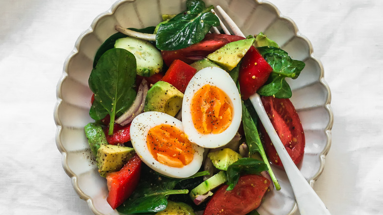 hard boiled egg with salad made of spinach, tomato, cucumber, and avocado