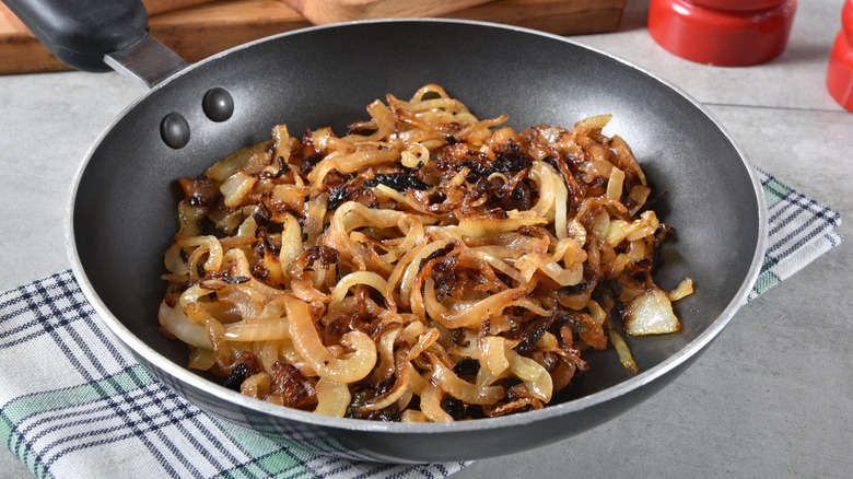 Pan of caramelized onions on a plaid towel on a light gray countertop.