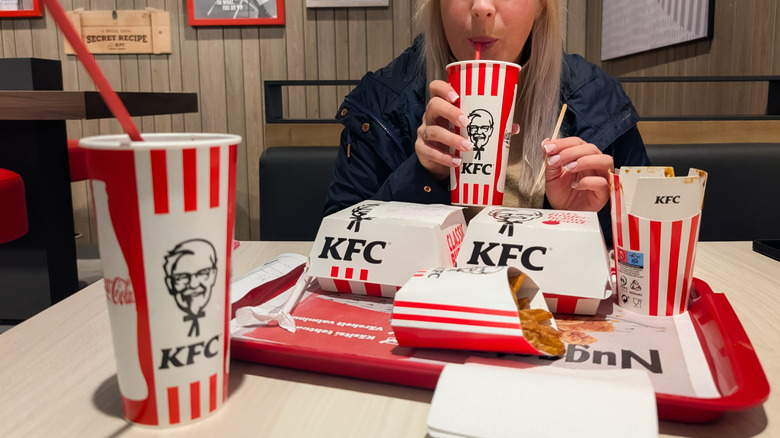 A person with a tray of KFC items in front of her sipping a KFC beverage