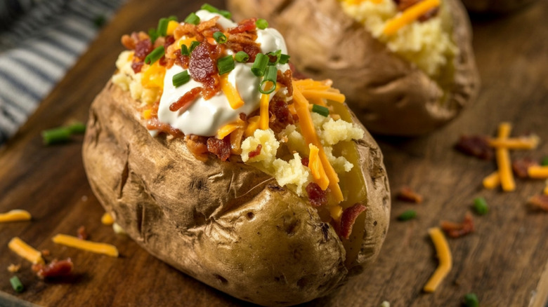 Loaded baked potato with bacon, chives, cheese, and sour cream on wood board.