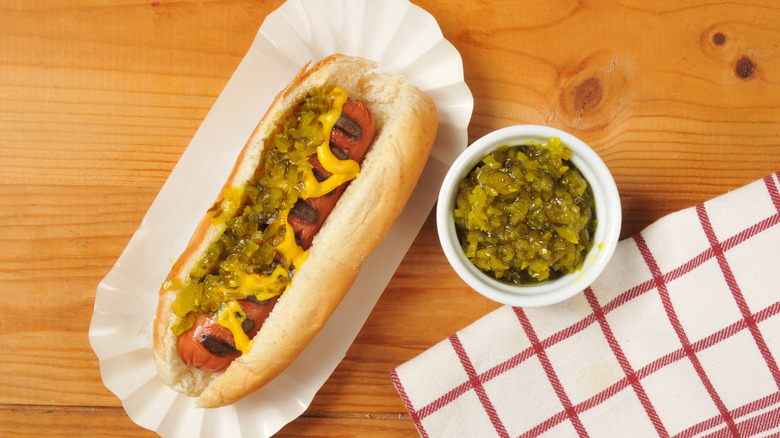 Hot dog with mustard and relish, with dish of relish on the side.