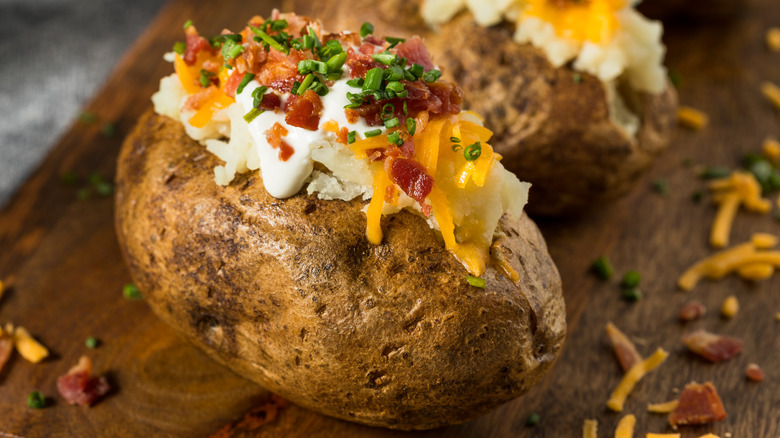 A baked potato with cheese, sour cream, bacon, and chives on a wooden board