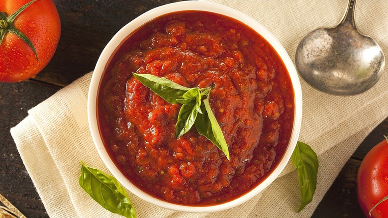 Top-down view of tomato sauce in a white bowl with fresh basil leaves