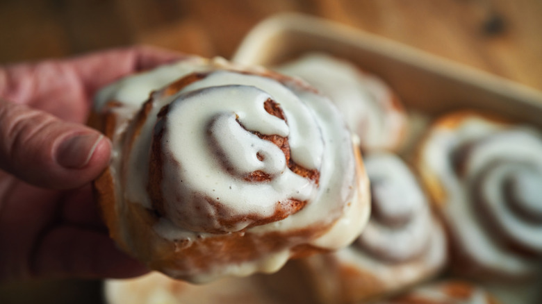 Hand holding a cinnamon roll.