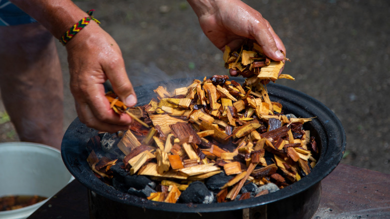 adding soaked woodchips to a charcoal smoker