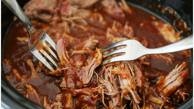 Pork  being pulled apart with two forks in a pot