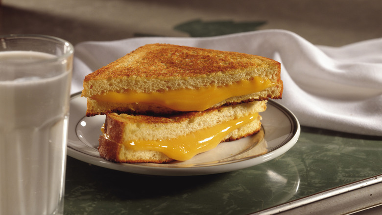 Grilled cheese sandwich cut in half with the halves stacked on a white plate next to a glass of milk and a cloth napkin