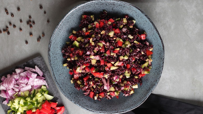 Cooked black rice with fresh chopped tomatoes, cucumbers, and red onion in a shallow gray plate