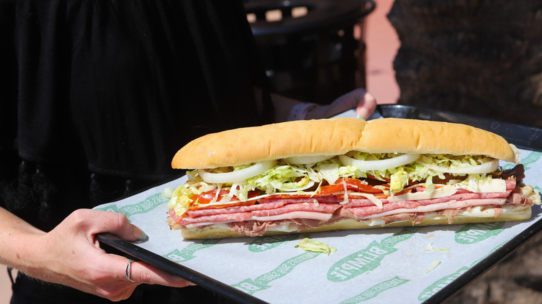 A person holding a tray with a Blimpie sub
