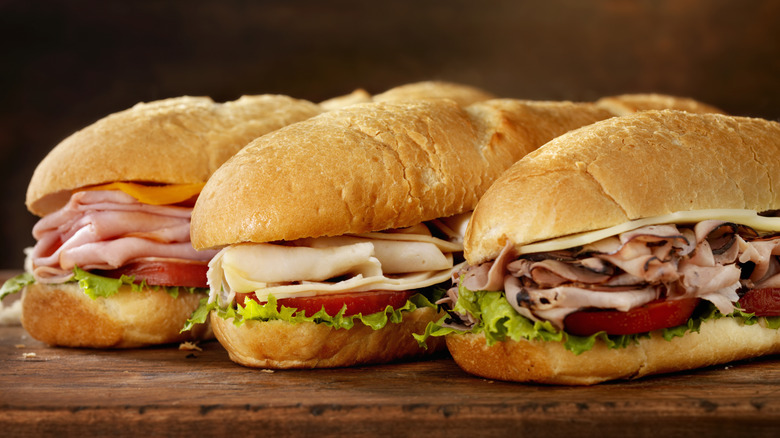 Three sub sandwiches on a wooden cutting board