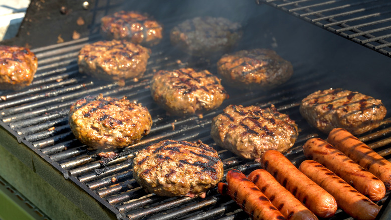 Hot dogs and hamburgers cook on an outdoor grill.
