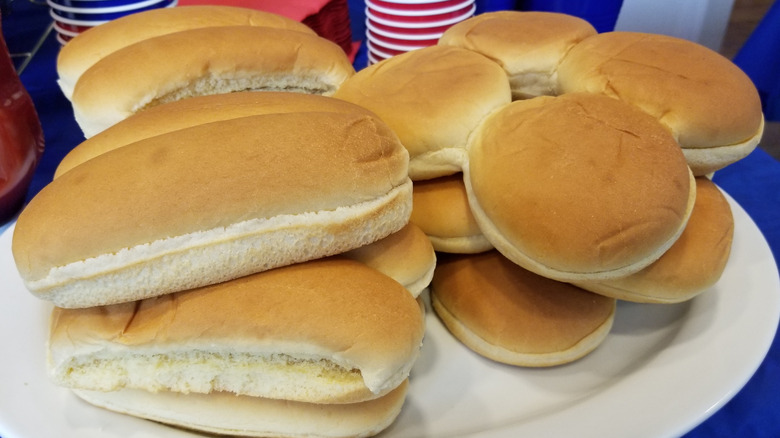 Hot dog buns and hamburger buns are stacked on a plate.
