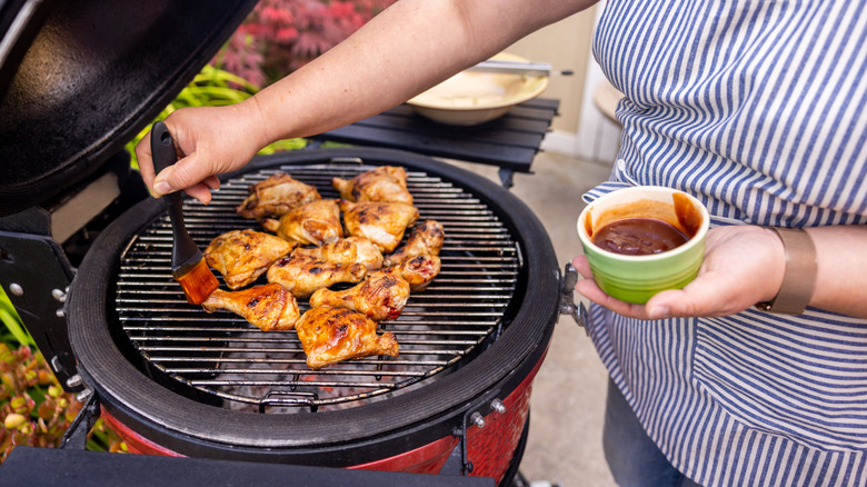 A person's hand is seen basting barbecued chicken on the grill.
